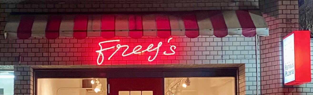 赤と白のストライプの日よけの下に光る赤いネオンの「Frey's」。右に「Famous Pizzeria」と書かれた赤い突き出し看板。