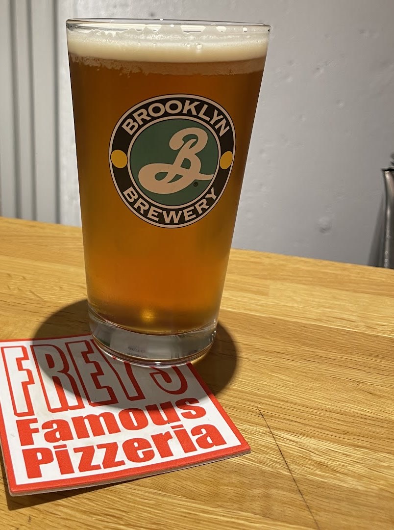 赤と白の「FREY'S Famous Pizzeria」のコースターにのった琥珀色のビールのパイントグラス。